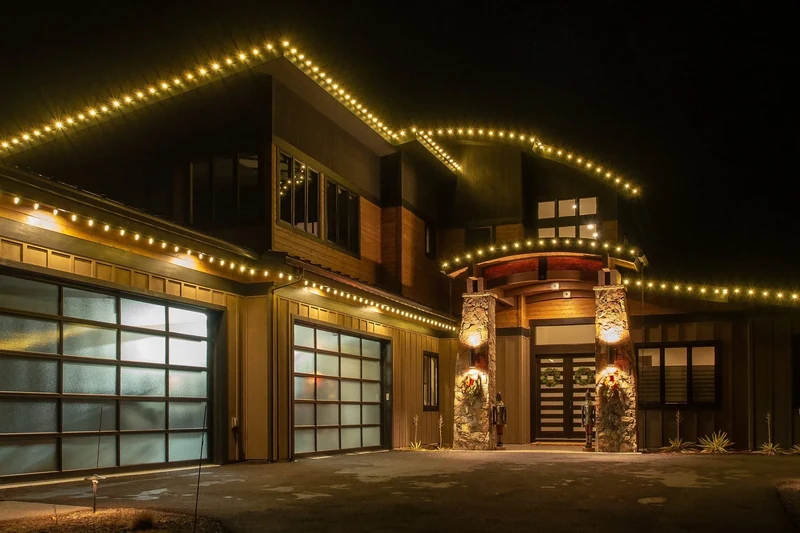 Commercial building with warm white Christmas lights tracing the full roofline and lit garland at the entrance