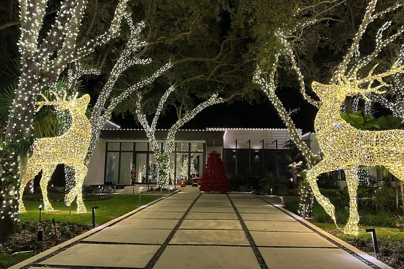Commercial entry walkway lined with warm white wrapped trees and two large lit reindeer figures flanking the path