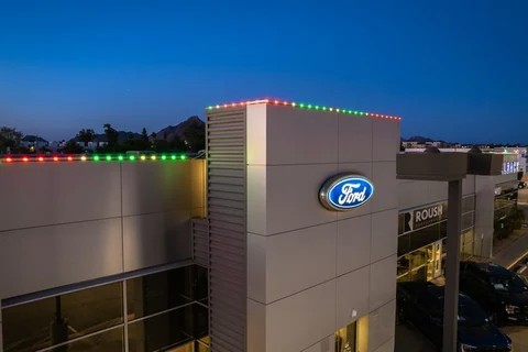 Car dealership building outlined in red and green lighting along the parapet edge at dusk