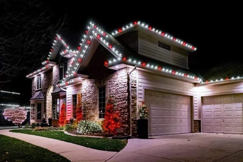 Family home outlined in alternating red, white and green Christmas bulbs across the rooflines with lit landscaping below