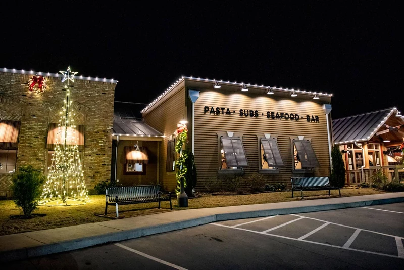 Restaurant exterior with a lit Christmas tree at the entrance and warm white wrapped trees along the walkway