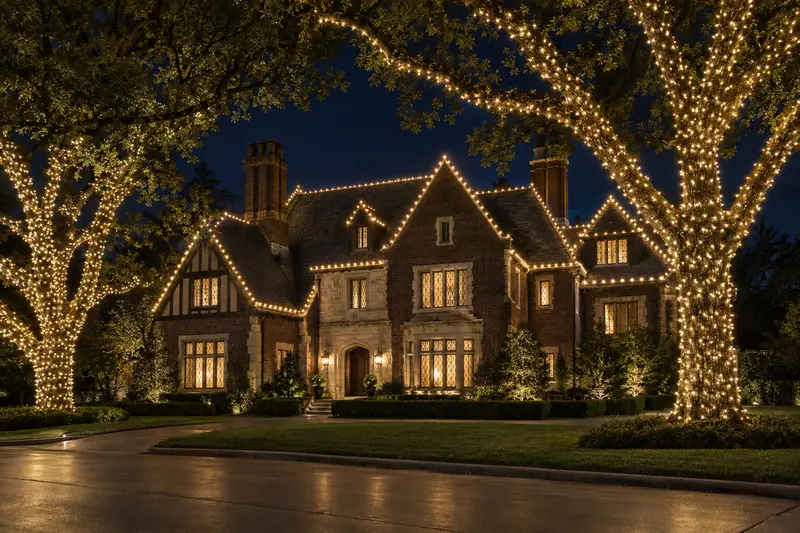 Brick Tudor home in Highland Park TX outlined in warm white Christmas lights at blue hour