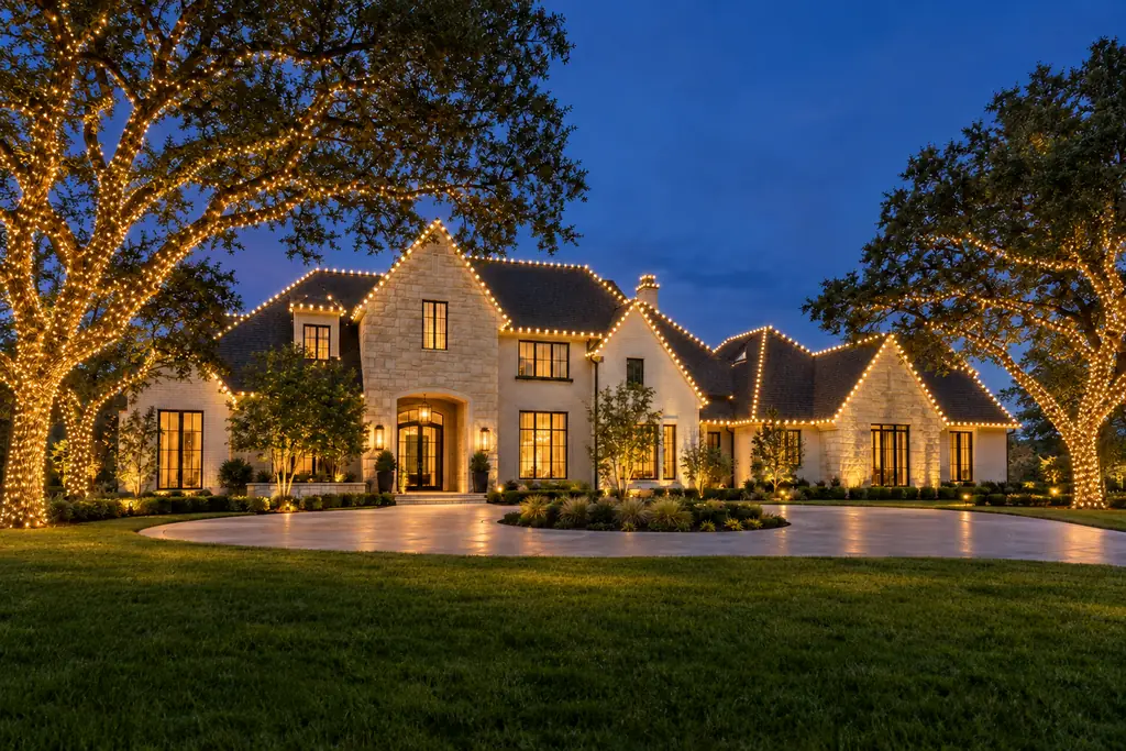 The same Dallas–Fort Worth home with warm white Christmas lights lit along the roofline and trees